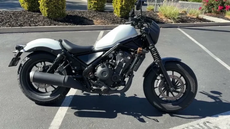 Side profile view of the newly unveiled Honda Rebel 500 cruiser motorcycle parked outdoors, featuring a white fuel tank, black frame, and bobber-inspired styling.